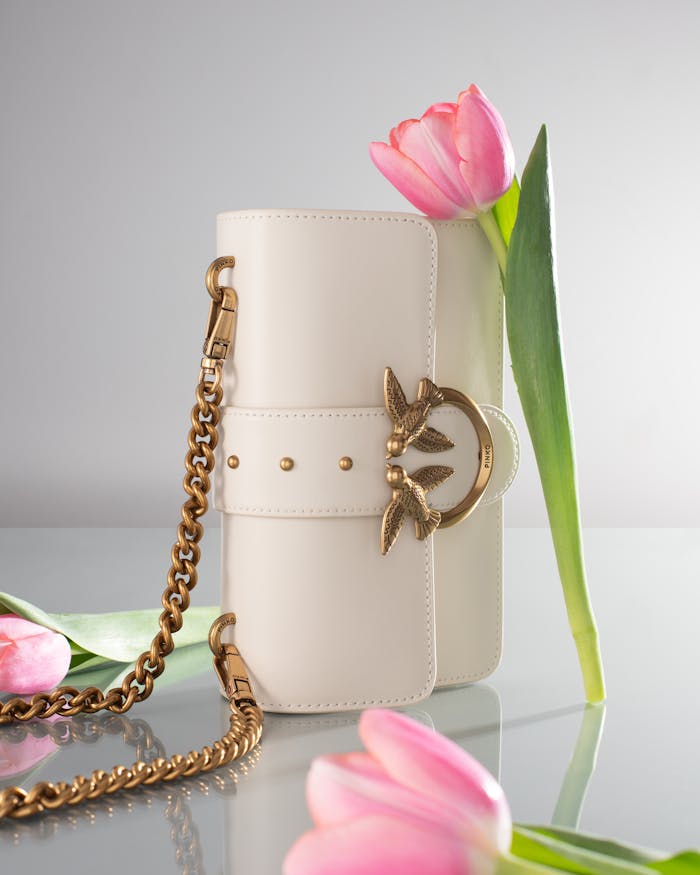 services-img Classy white handbag with gold chain and tulip decorations on a reflective surface.
