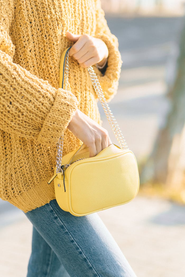 services-02 A stylish yellow bag paired with a knitted sweater and denim jeans outdoors.